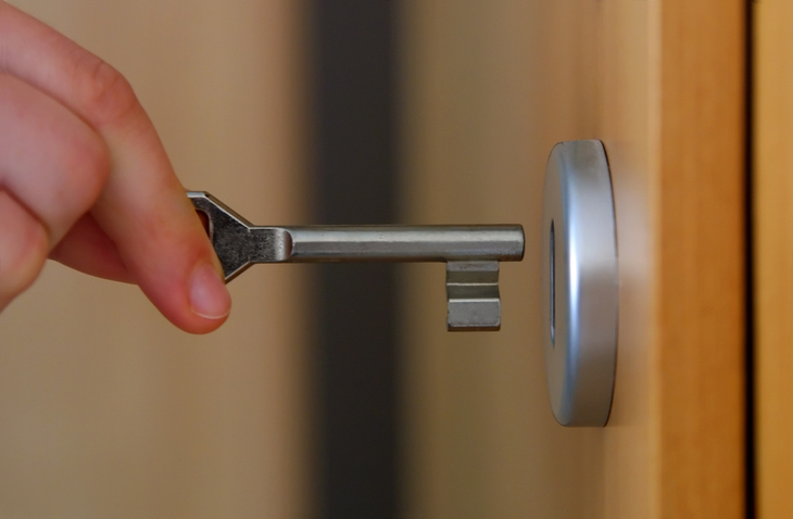 A hand inserts a key into a lock on a door