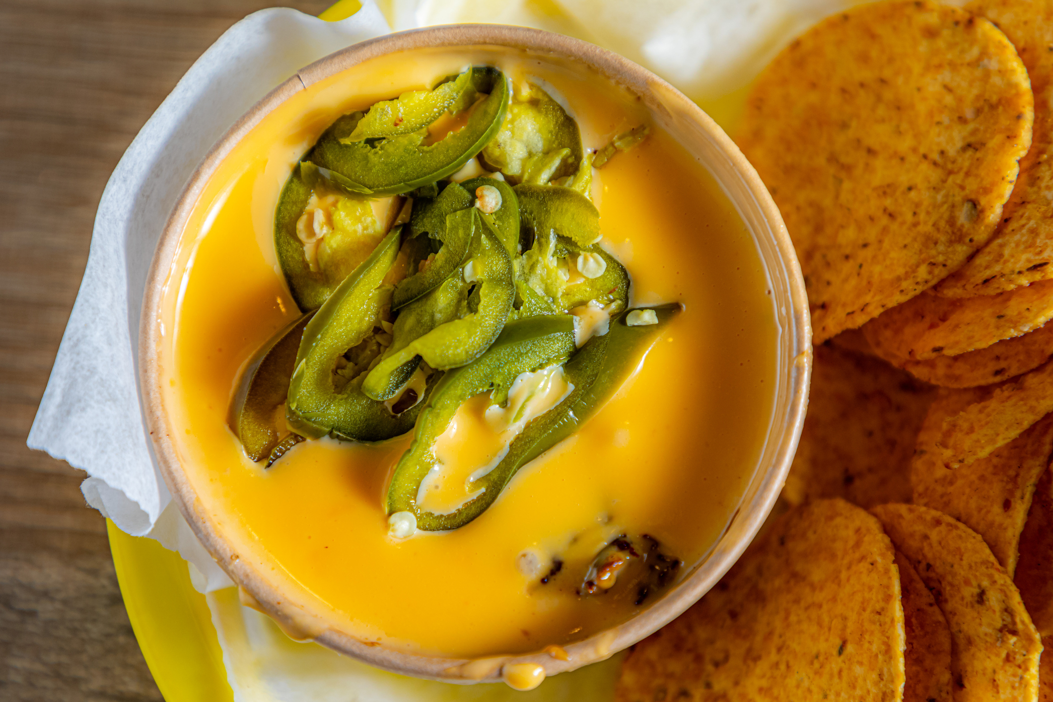 A bowl of nacho cheese dip topped with sliced jalapeños next to a pile of tortilla chips