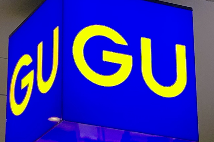 A blue, hanging sign with the letters &ldquo;GU&rdquo; in yellow, displayed twice on two sides of the cube