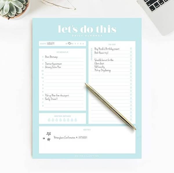 Daily planner showing a to-do list, schedule, hydration tracker, and notes, with a pen on it; includes tasks like grocery shopping and birthday reminders