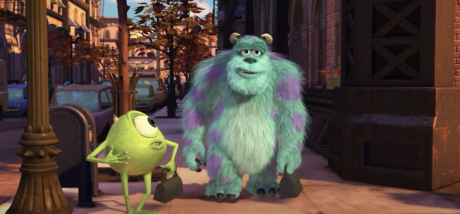 Mike Wazowski, a one-eyed green monster, and Sulley, a large furry monster, walk together on a sidewalk in a bustling city scene from Monsters, Inc