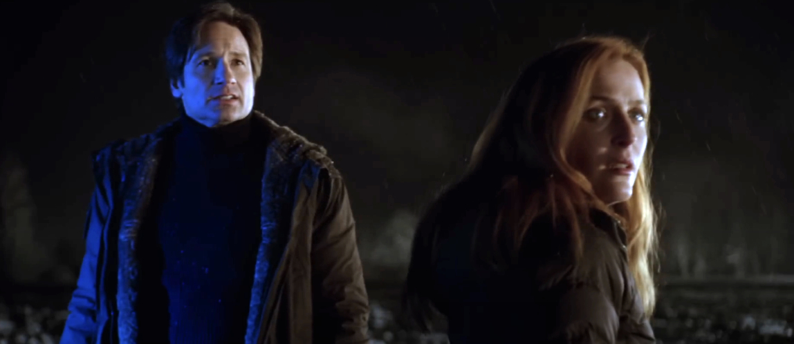 David Duchovny and Gillian Anderson stand outdoors at night, looking concerned