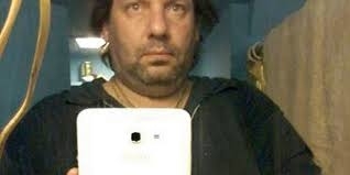 Adam Strong takes a selfie in a mirror with a tablet, wearing casual clothing