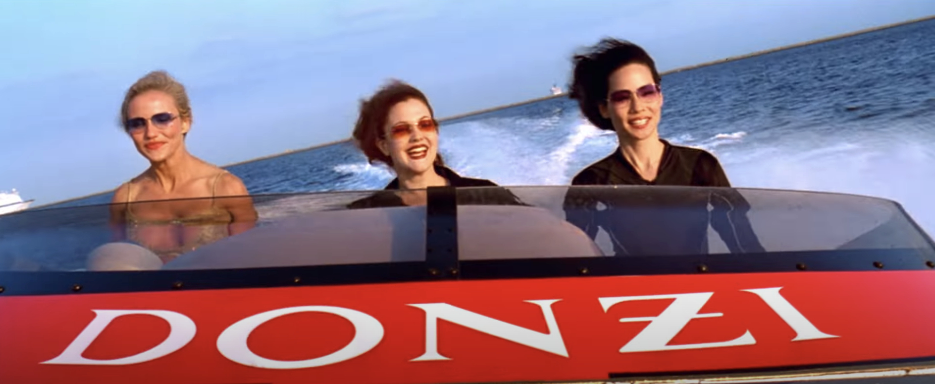 Cameron Diaz, Drew Barrymore, and Lucy Liu ride in a speedboat labeled "Donzi" on the water, smiling and wearing sunglasses