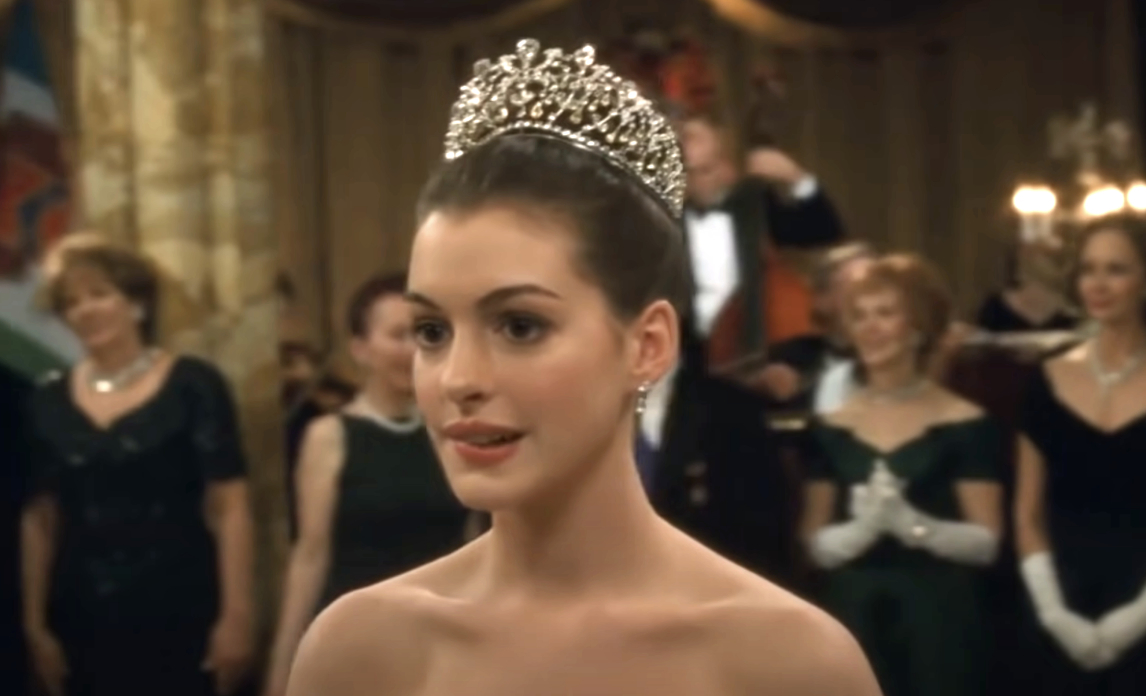 Anne Hathaway as Mia Thermopolis in The Princess Diaries, wearing an elegant white gown and a sparkling tiara, surrounded by formally dressed attendees
