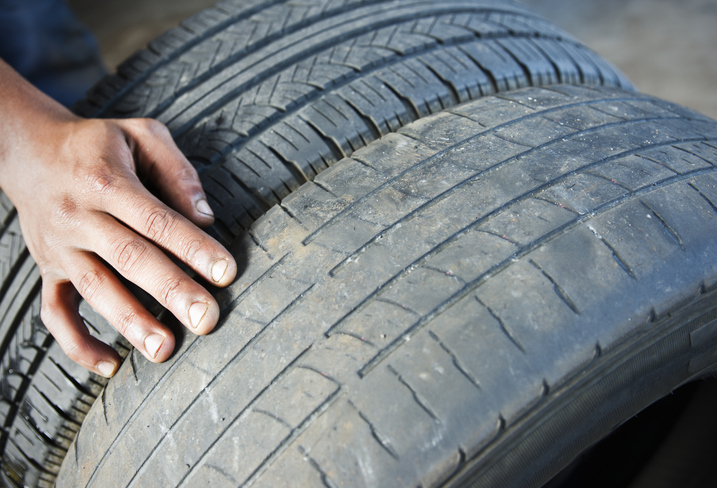 Close-up of a person's hand touching the treads of two car tires, showing a comparison between a worn tire and a new tire