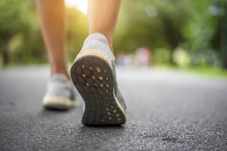 A close-up of a person walking on a paved path wearing athletic shoes, with a green, blurry background