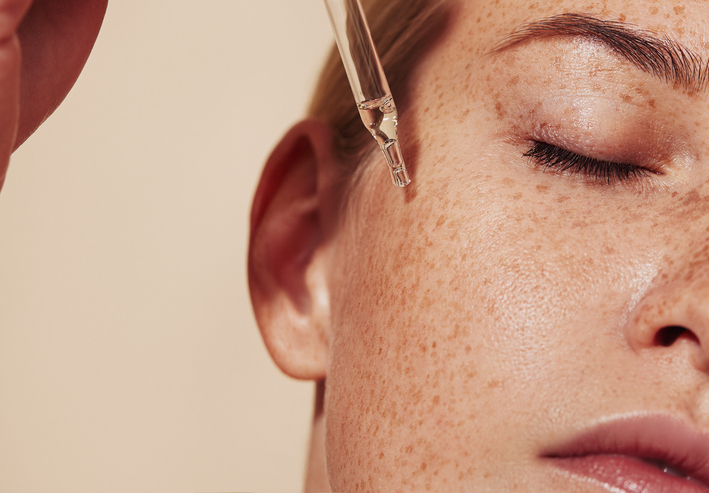 Close-up of a person applying skincare serum to their face with a dropper