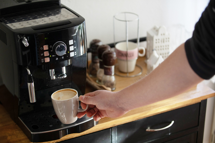 A person's arm holding a cup under the dispenser of a coffee machine on a countertop with various coffee-related items