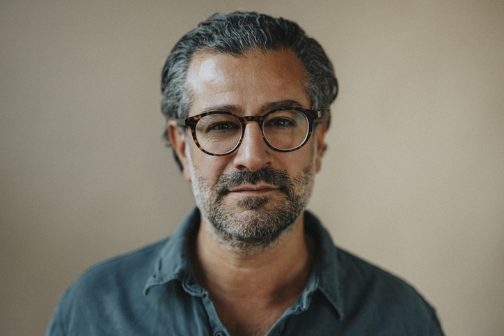 A man with glasses and salt-and-pepper hair wearing a collared shirt poses for a portrait