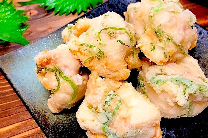 黒いお皿に盛り付けられた白っぽい揚げ物の料理と、背景に置かれた青じその葉。
