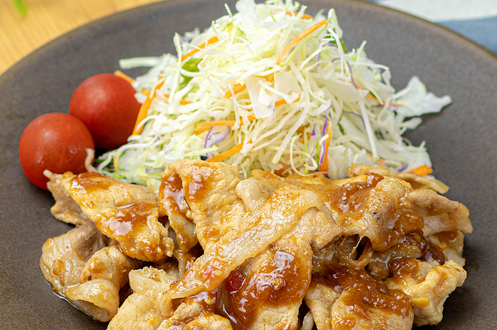 お皿に盛られた照り焼きポーク、千切りキャベツとミニトマトが添えられている。