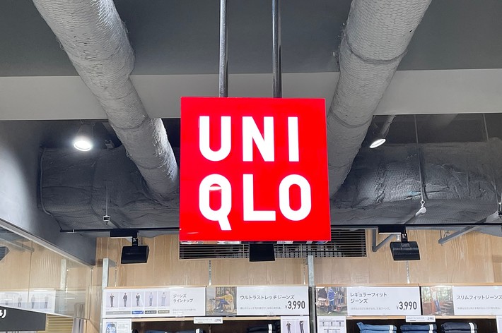 ユニクロ店内の天井から吊り下げられた赤いUNICLOの看板。背景に商品棚が見える。