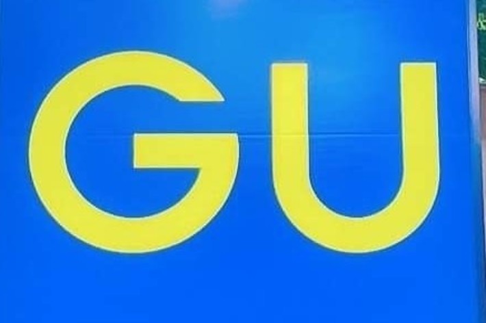 A large sign with bold yellow letters &ldquo;GU&rdquo; is displayed against a background with reflective surfaces and trees visible