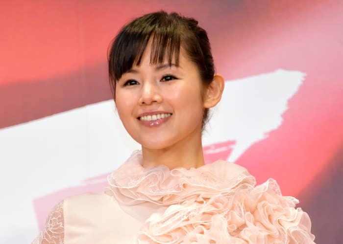 女優の上白石萌音がレースのディテールが特徴的なエレガントなドレスを着て、微笑んでいる。