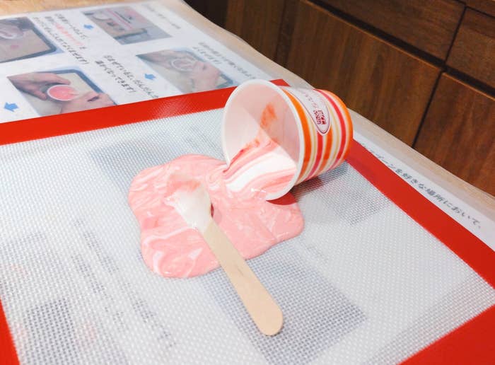 倒れたカップからピンク色のアイスクリームが溶け出し、アイスの棒が手前に置かれている。