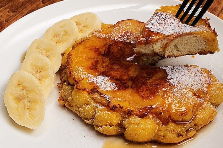 フォークで一口分を切り取ったバナナの添えられたパンケーキ。シロップと粉砂糖がかかっている。