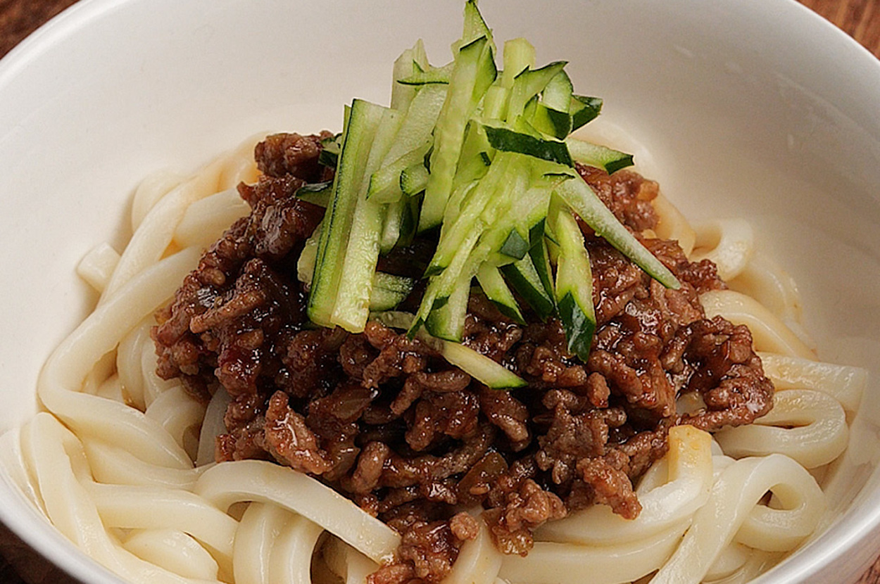 うどんが入ったボウルの中に、肉みそと細切りのきゅうりが乗せられた料理。