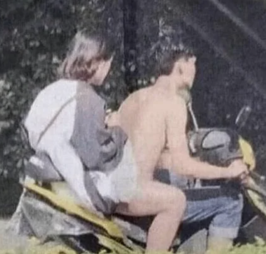 A man and a woman are riding a motorcycle together. The man is shirtless, and the woman is in casual attire with a backpack. Their faces are not visible