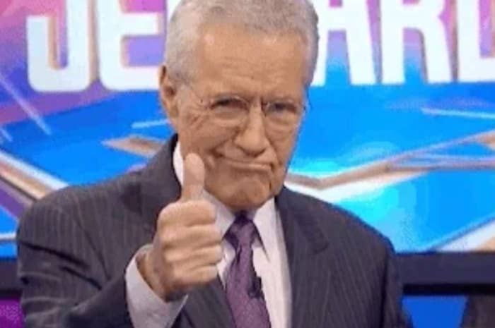 Alex Trebek giving a thumbs up   portion    lasting  successful  beforehand   of the "Jeopardy!" logo. He is wearing a suit   and a tie