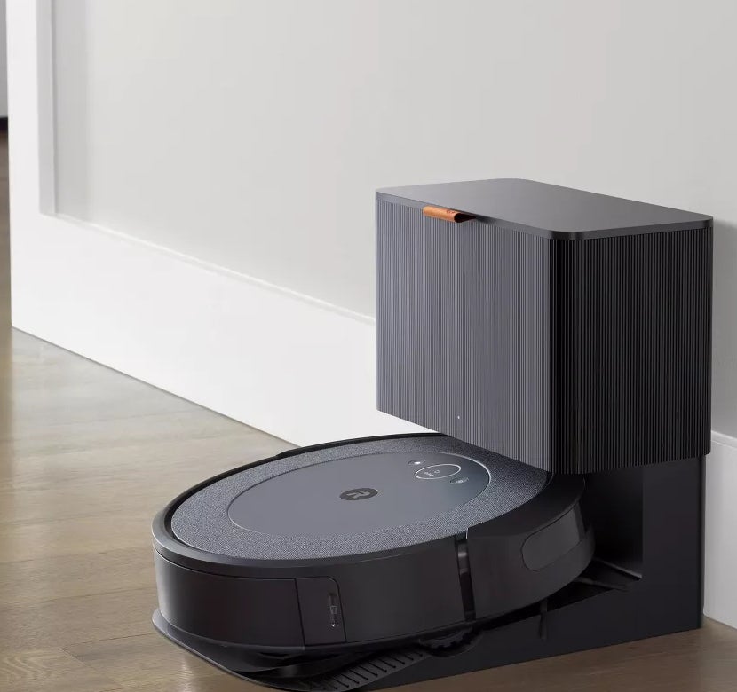 A robot vacuum cleaner is docked at its charging station against a wall on a hardwood floor