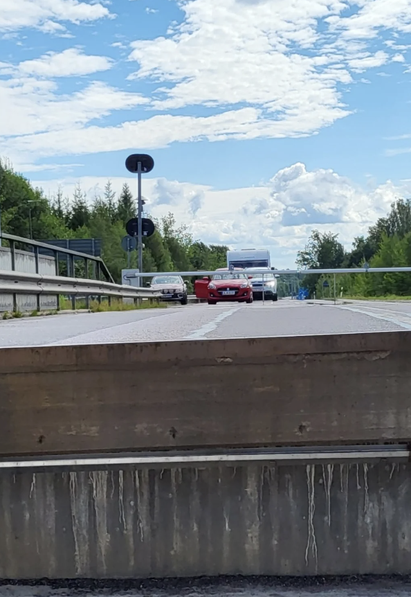 A busy road scene with several cars driving, including a red sports car and a white truck. The sky is partly cloudy