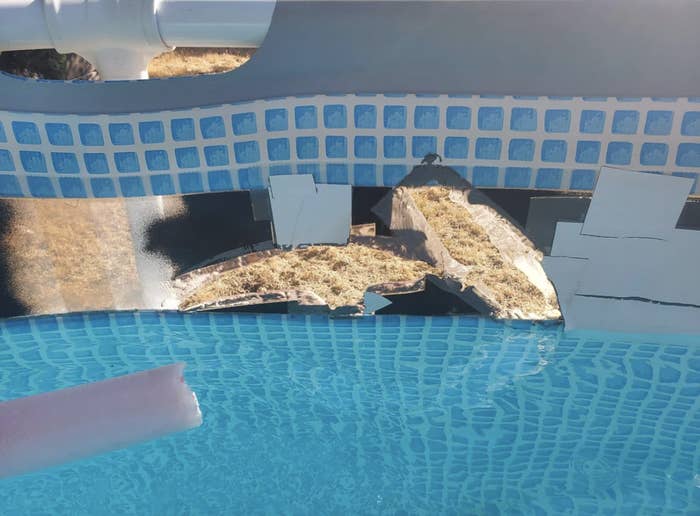 An above-ground pool with a large, patched-up tear in the wall, revealing the outside grass and ground through the damaged section