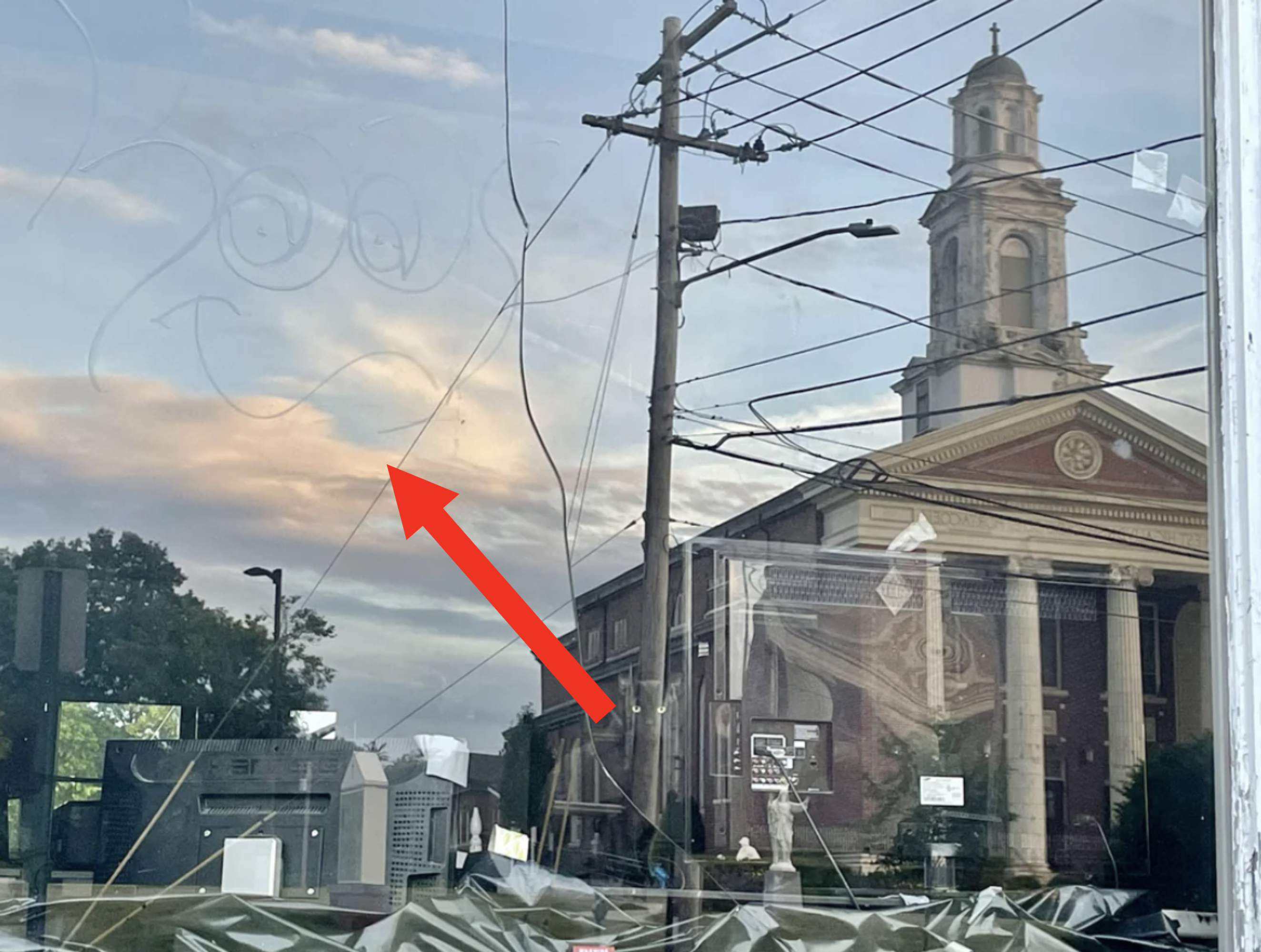 A cracked window reflects power lines and a church with a bell tower in a suburban area at dusk