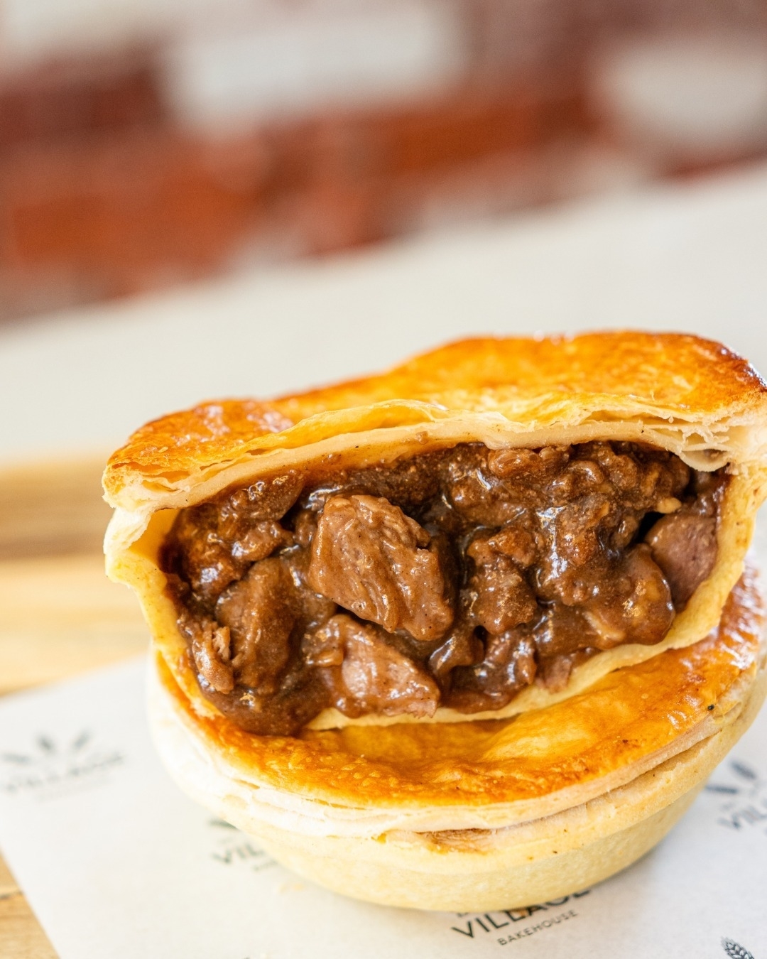 A close-up of a meat pie with a flaky crust, showcasing chunks of meat and savory filling. The pie rests on a printed paper napkin