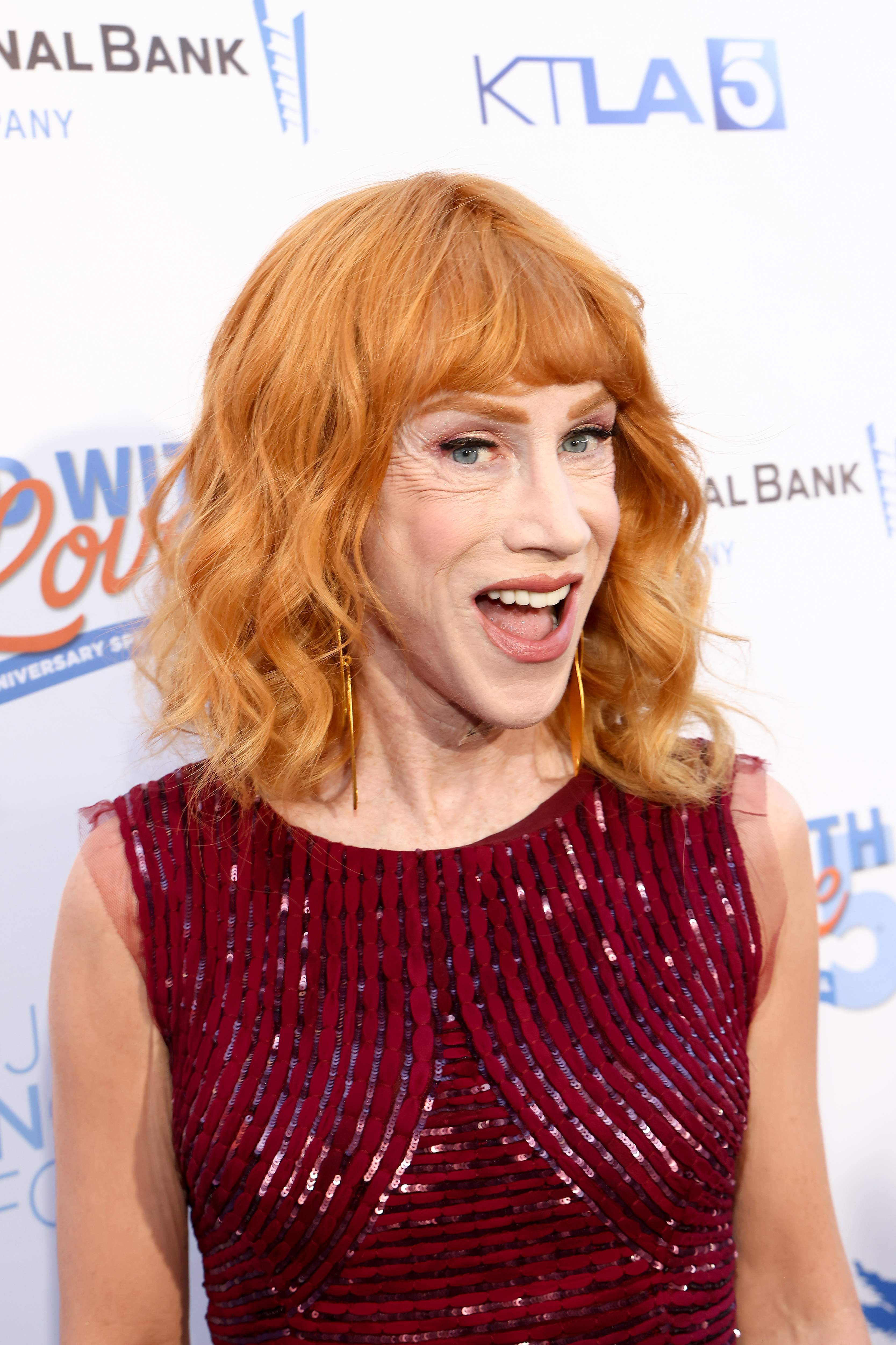 Kathy Griffin, wearing a sleeveless, sequined dress, smiles on the red carpet at a National Bank event