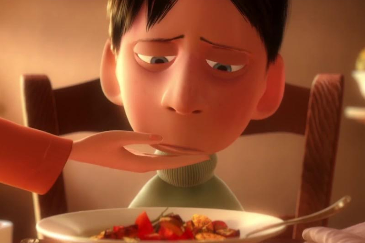Animated character Alfredo Linguini from Ratatouille nervously stares at a plate of food while a hand reaches towards his face