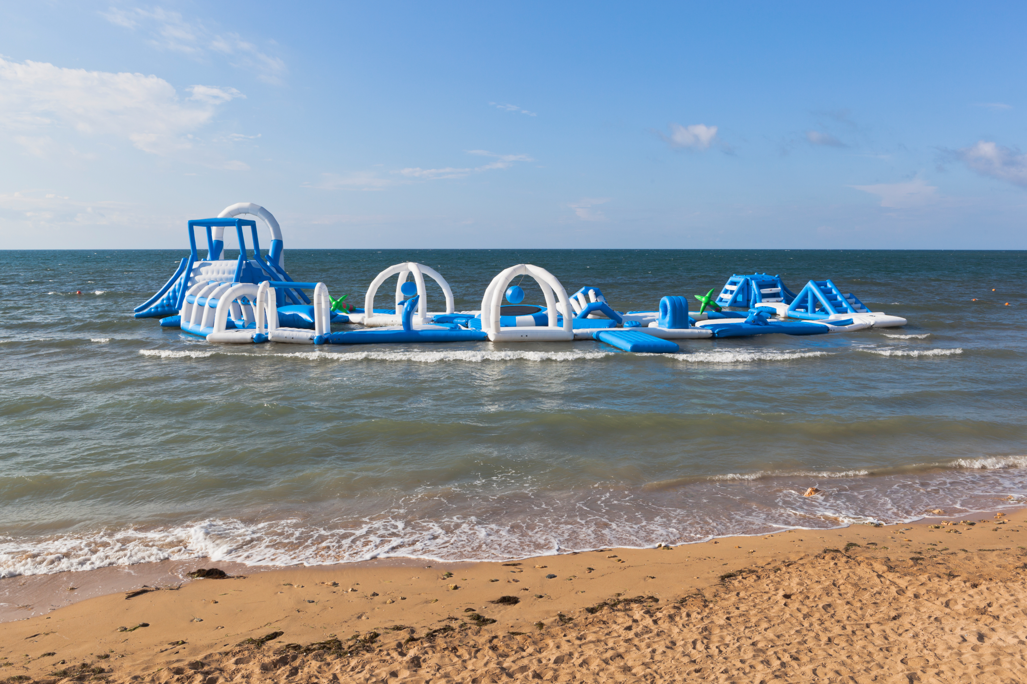 Inflatable water park with various obstacles and slides floating on the ocean near a sandy beach
