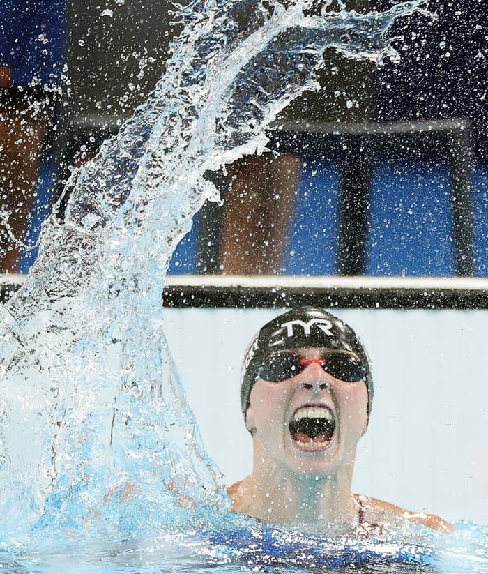 Swimmer celebrates in the pool amid splashing water, wearing a black swim cap and goggles