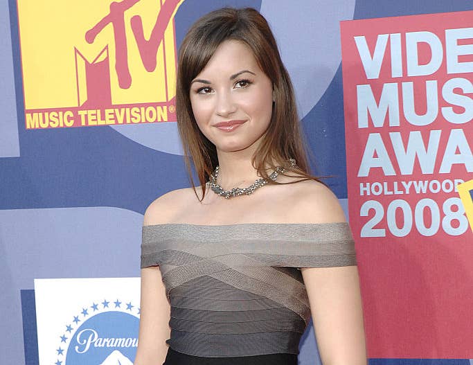 Demi Lovato on the red carpet at the MTV Video Music Awards 2008, wearing an off-the-shoulder, fitted dress with subtle horizontal stripes, accessorized with jewelry