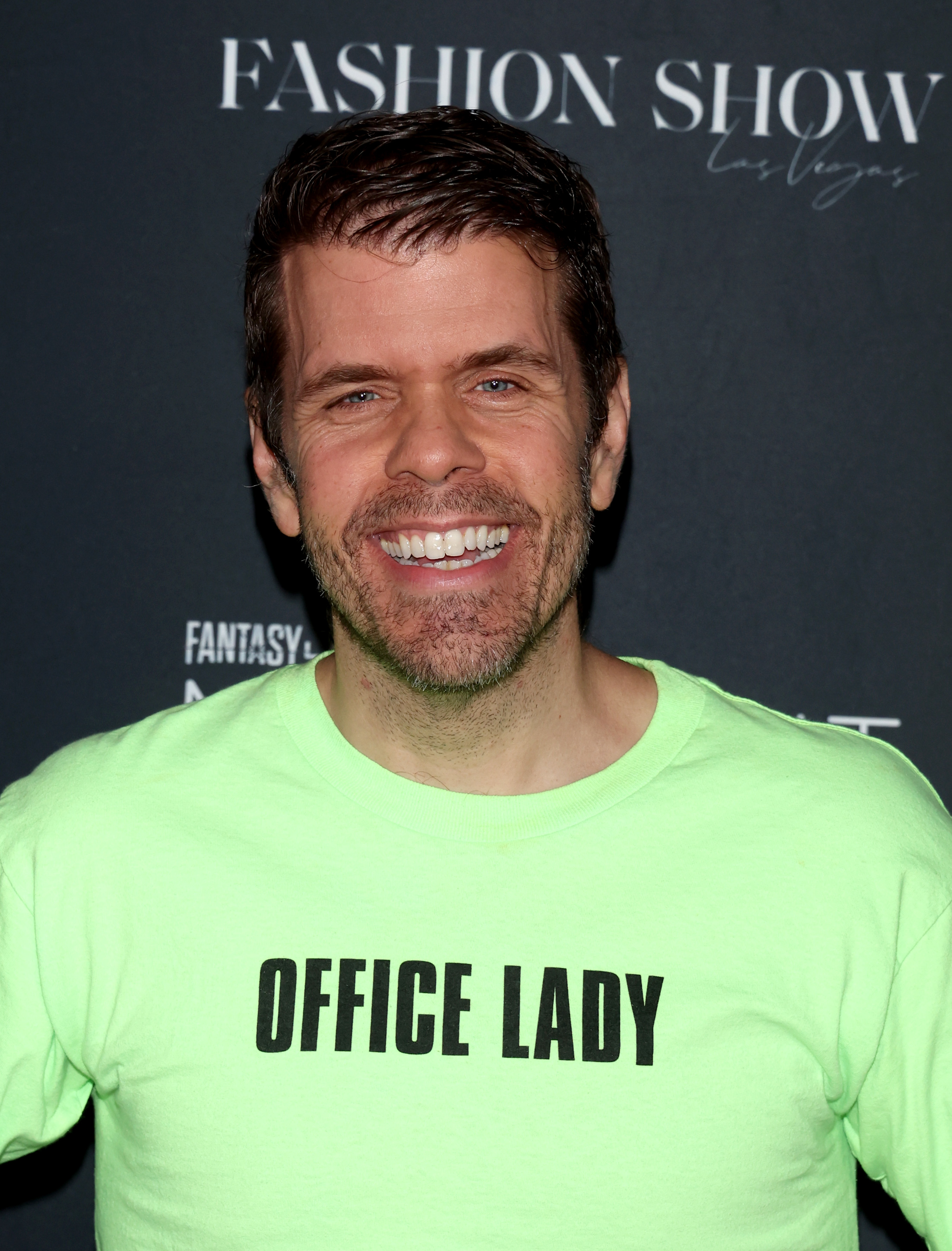 Perez Hilton smiles in a neon T-shirt with "OFFICE LADY" text at a Fashion Show event in Las Vegas