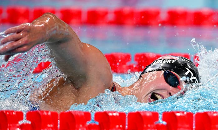 Katie Ledecky swims freestyle in a race, wearing a swim cap and goggles, surrounded by red lane markers