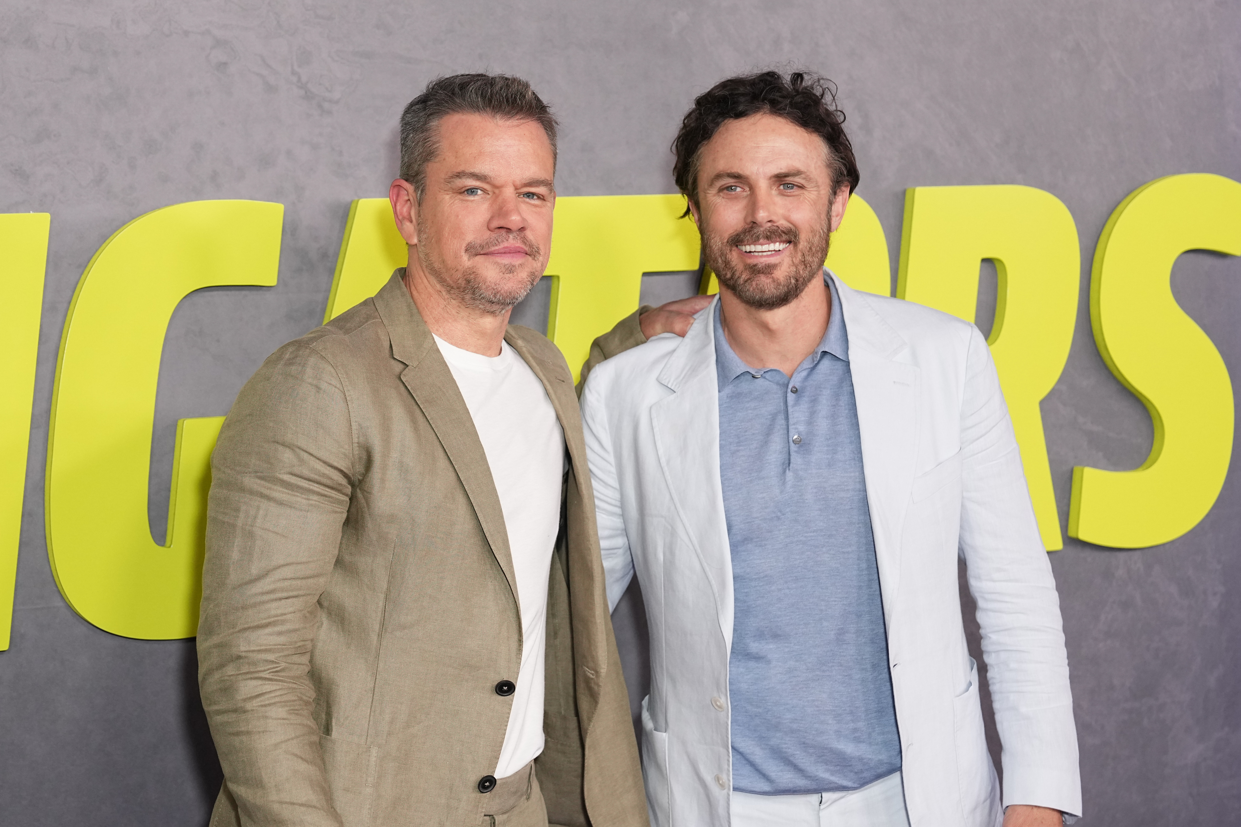 Matt Damon in a casual suit and white shirt posing with Casey Affleck in a light suit with a polo shirt at a movie premiere
