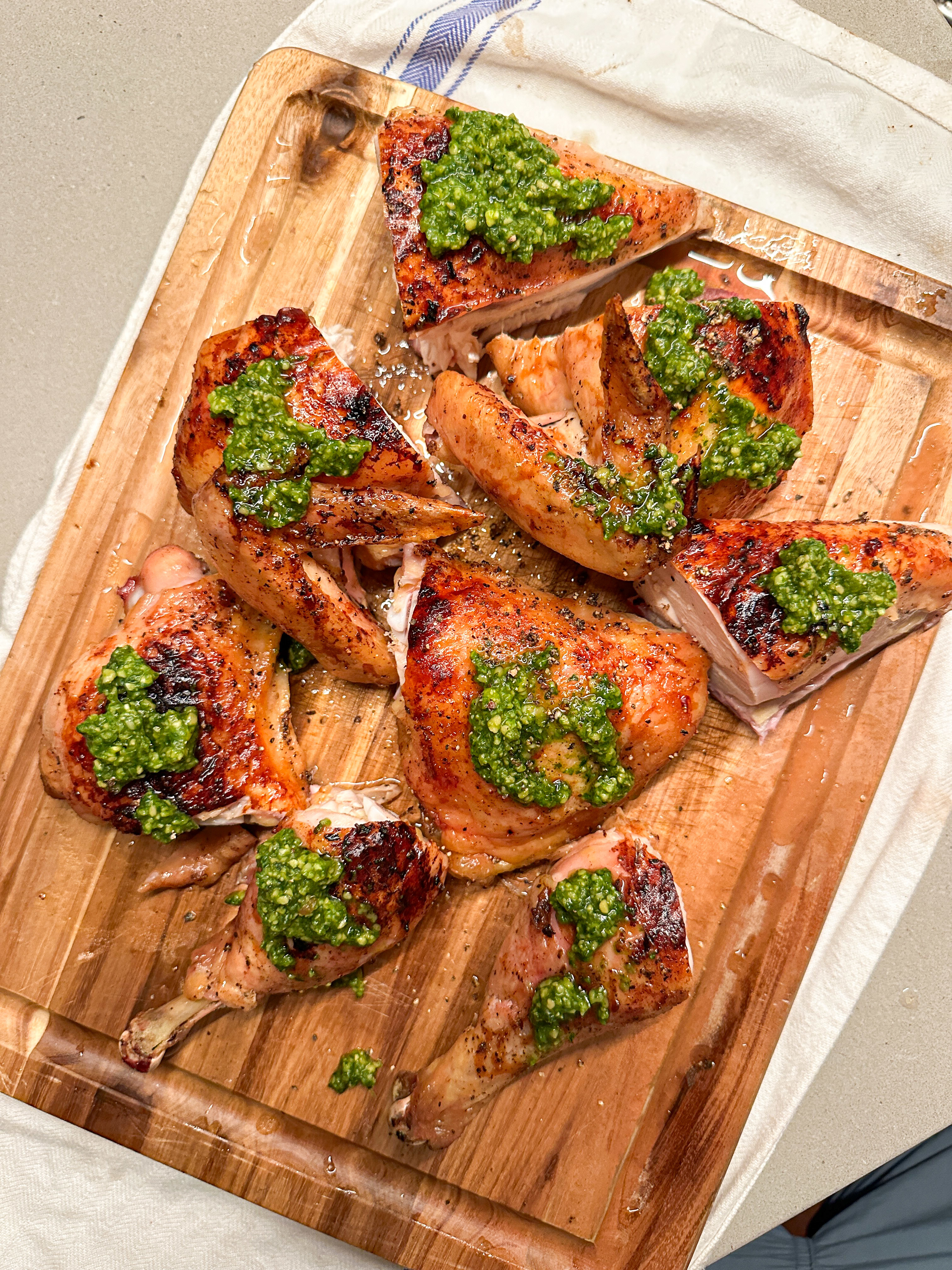 Grilled chicken pieces garnished with green pesto sauce on a wooden cutting board