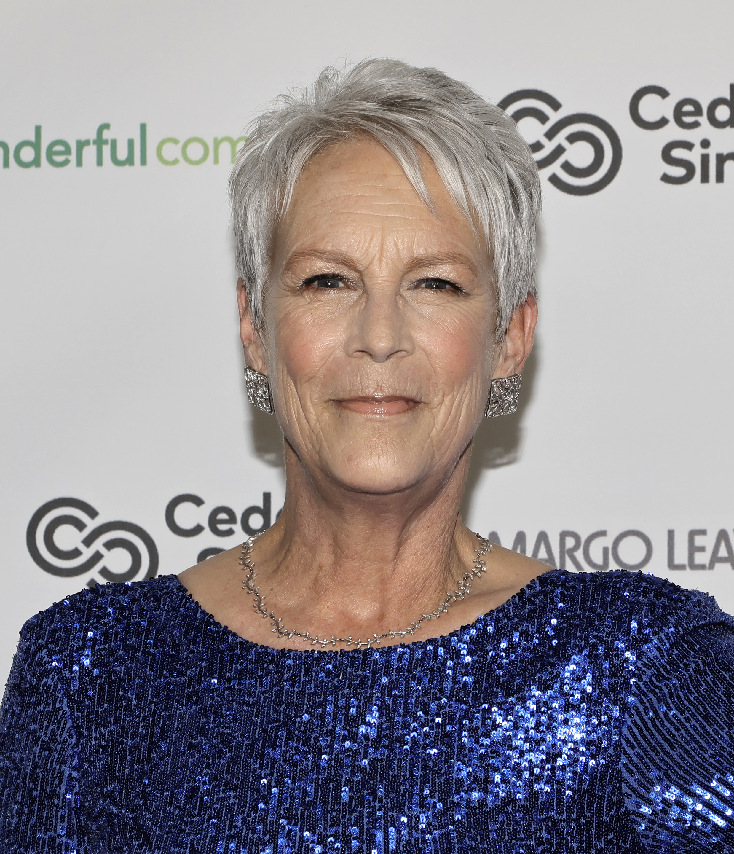 Jamie Lee Curtis smiles at a red carpet event, wearing a sequined dress and statement earrings