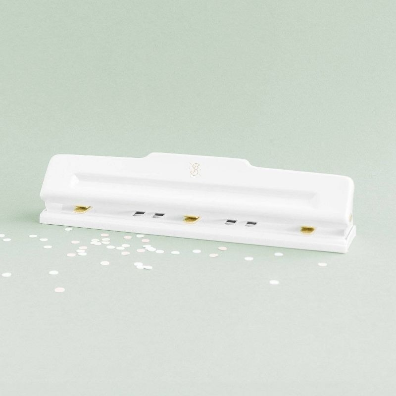 White paper hole puncher on a light green background with scattered paper hole cutouts