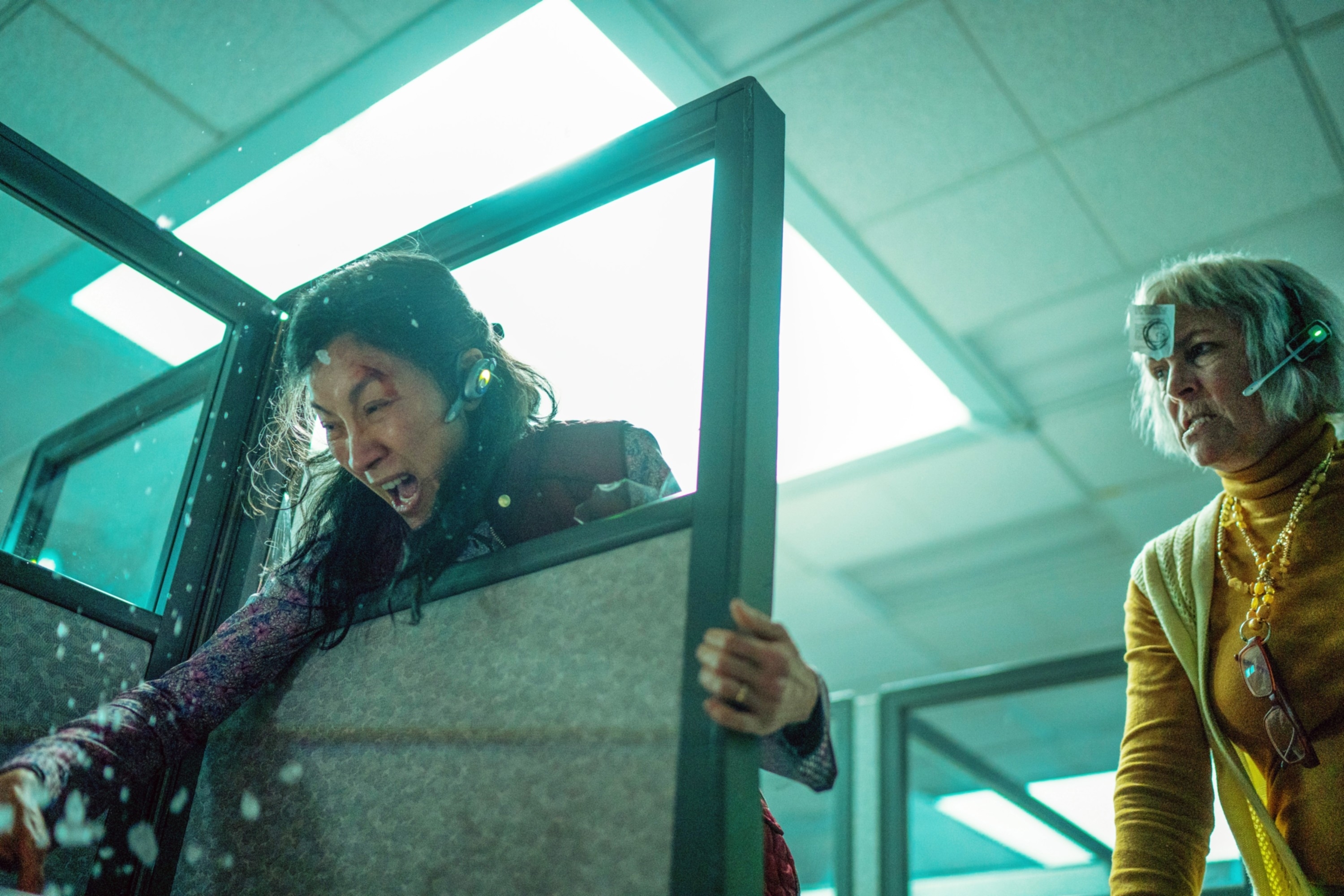 Michelle Yeoh and Jamie Lee Curtis in an office cubicle scene from the movie "Everything Everywhere All at Once," engaged in an intense action moment