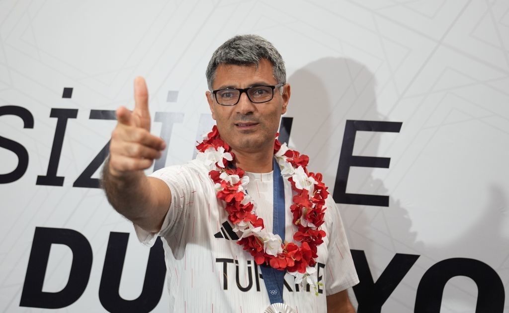 Yusuf Dikeç wearing a sports jersey with "Türkiye" and a flower garland necklace gestures with his right hand