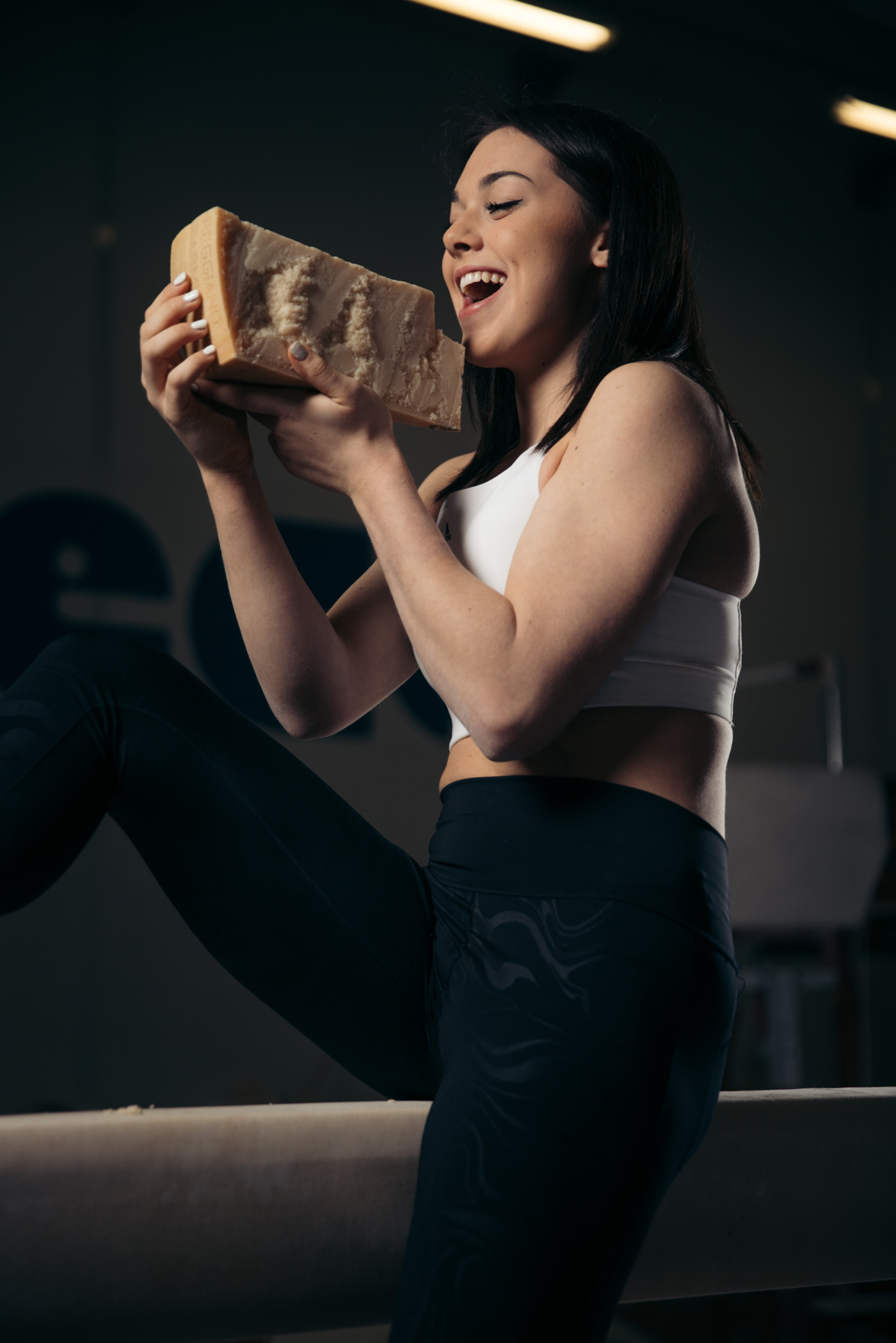 Simone Biles, dressed in a workout outfit, joyfully holding a carved block of cheese