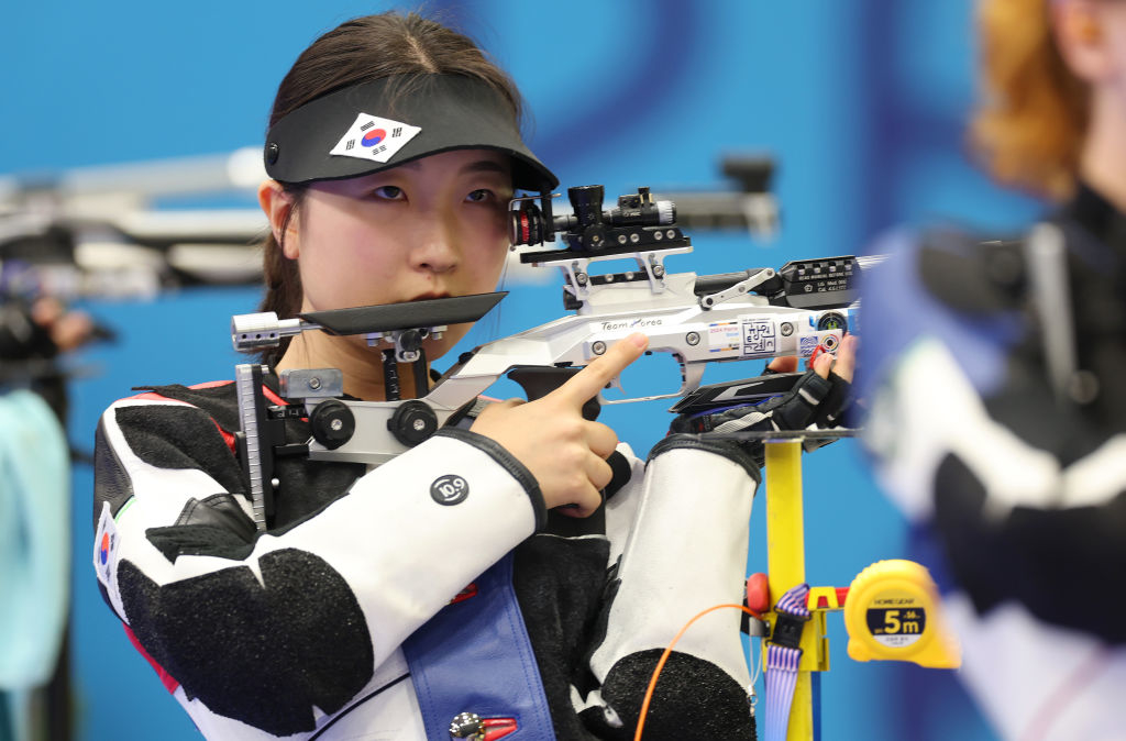 Han Ji-won focuses while aiming a rifle during a shooting competition. She's in black and white gear, including a cap with the South Korean flag