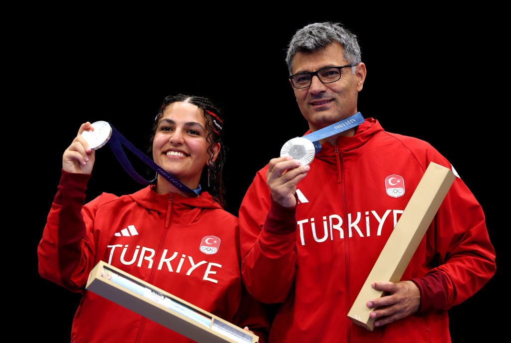 Sevval Ilayda Tarhan and Yusuf Dikec wear &quot;Türkiye&quot; jackets, holding silver medals and certificates, celebrating their achievement at a sports event