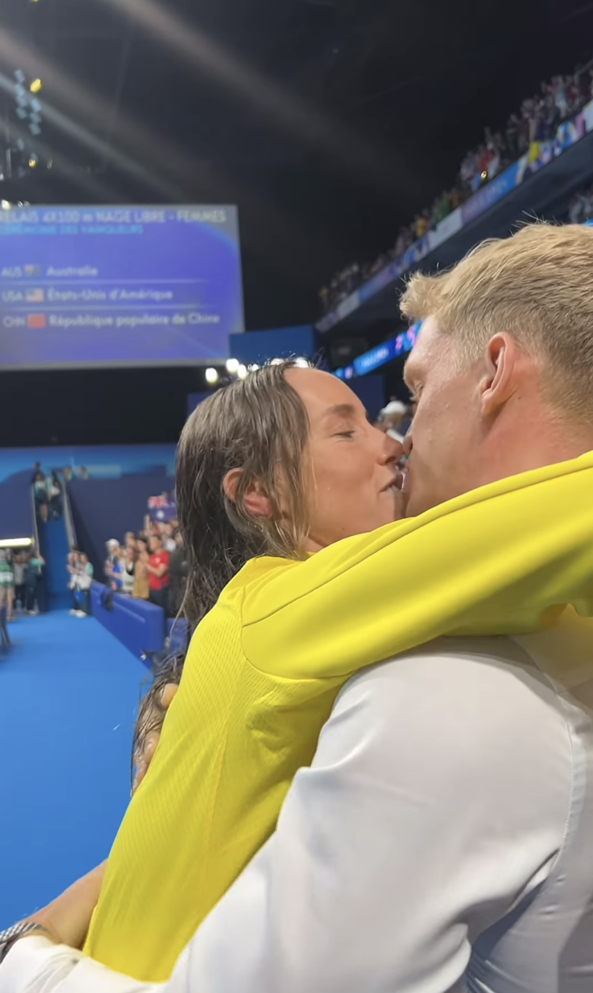 Emma and Cody put their arms around each other and kiss poolside. her hair is wet.