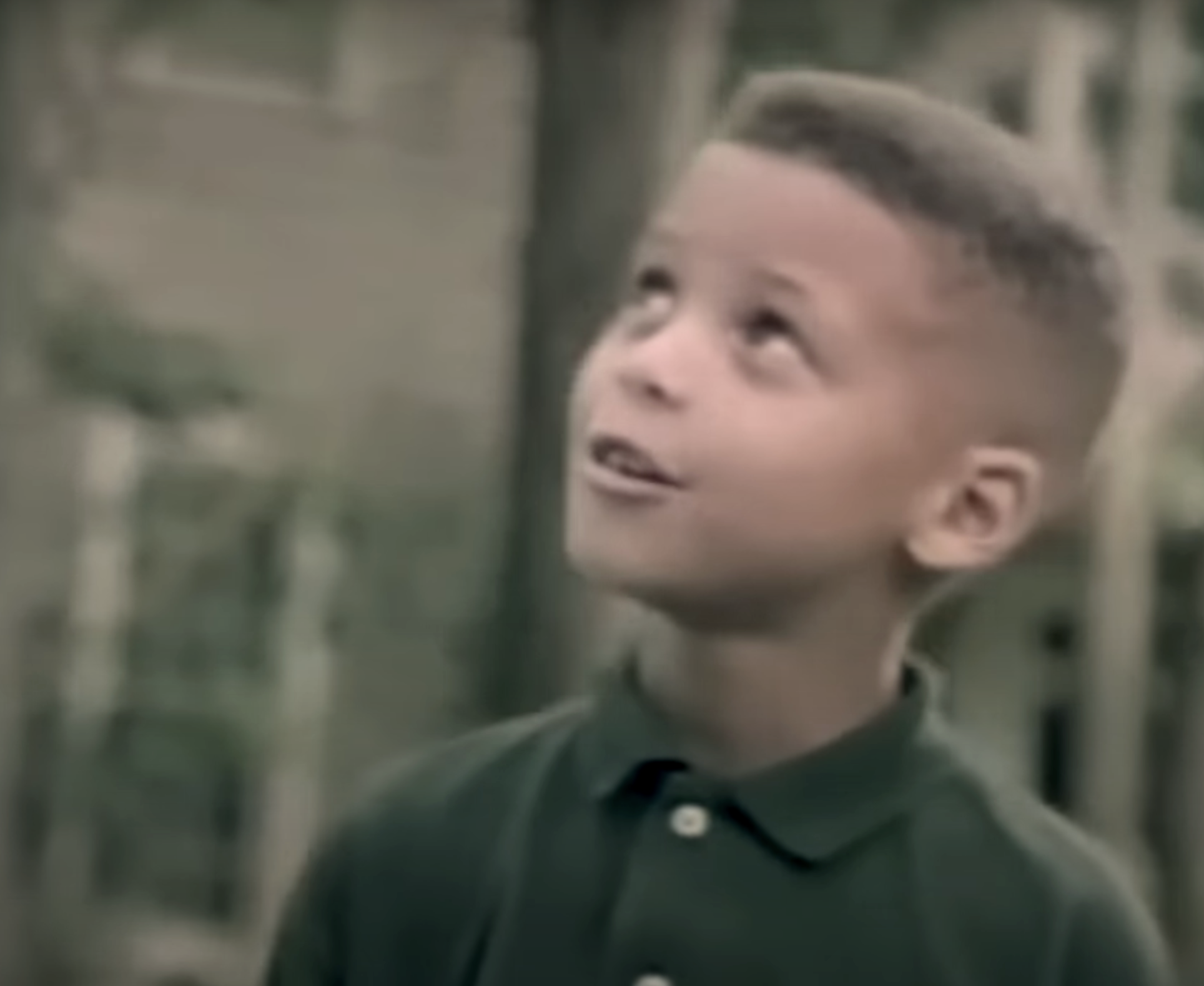 A young Stephen Curry, wearing a collared shirt, looks up with a curious expression while standing outdoors