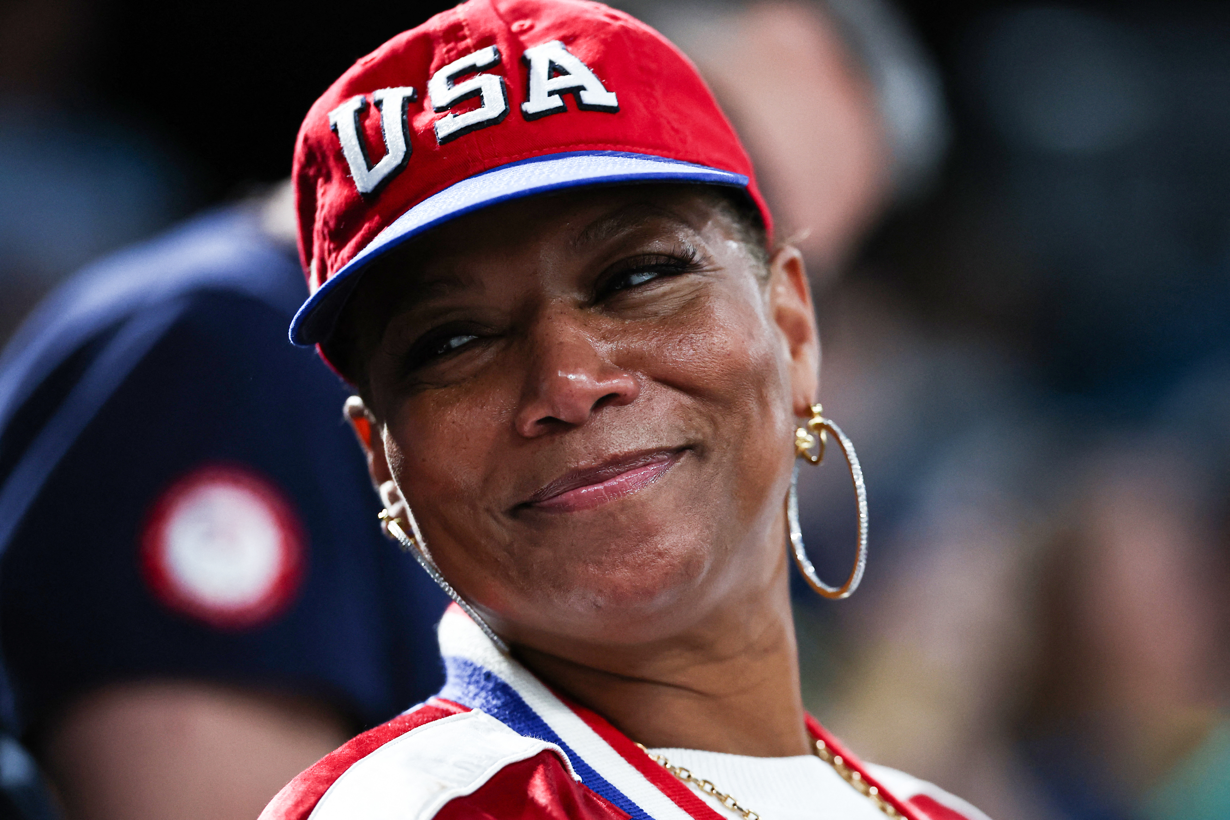 Queen Latifah wearing a USA cap and red sports jacket, smiling at an event