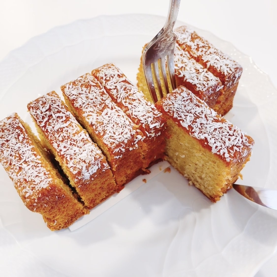 ココナッツがかかったスライスされたスポンジケーキがフォークで取り分けられている。
