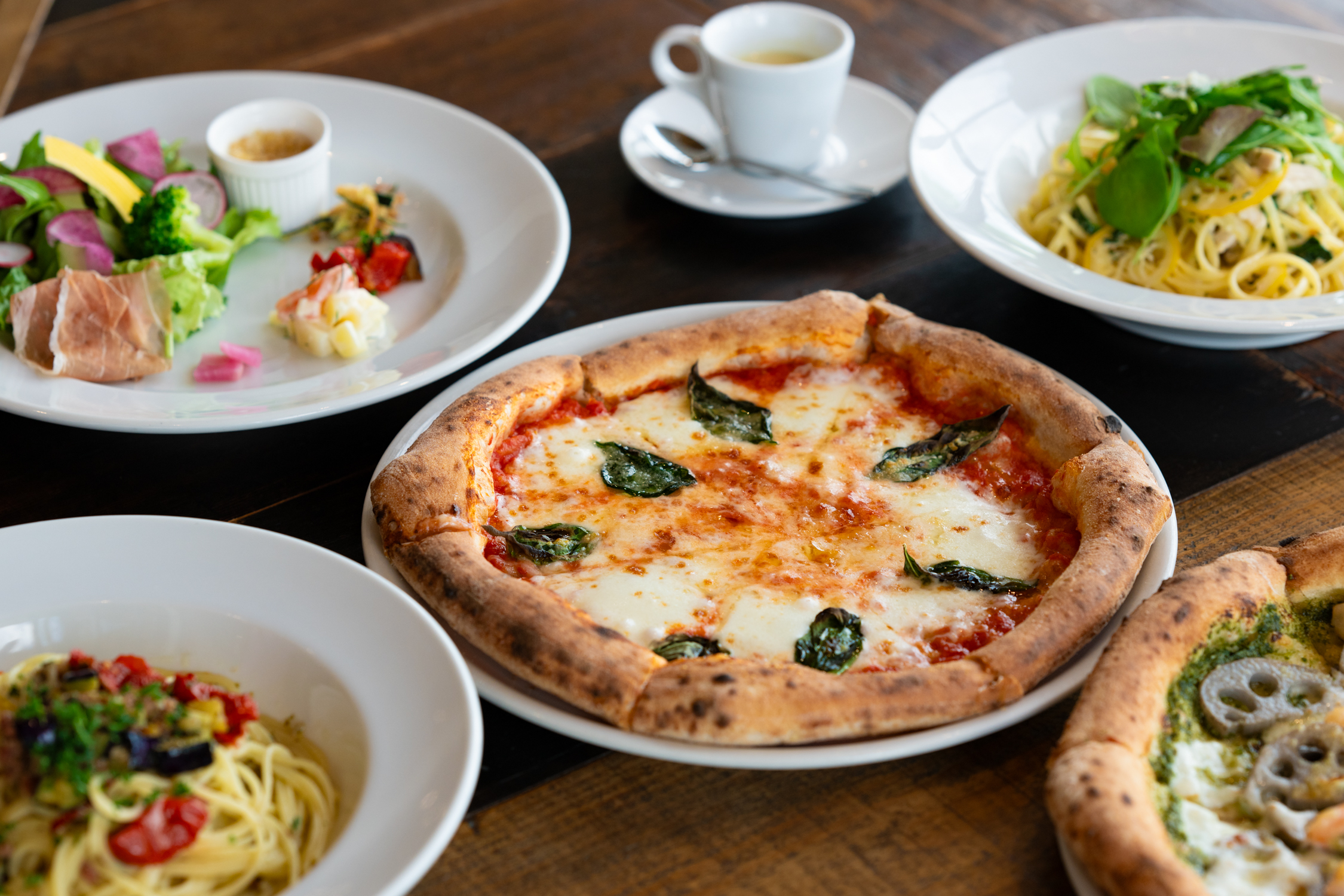 テーブルに置かれたピザ、パスタ、サラダ、エスプレッソの食事シーン。